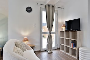 A modern living room with a sofa, a television on a wooden shelf, and a window with curtains.