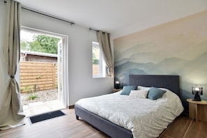 A bedroom with a bed, a nightstand, a wall-mounted lamp, and a view of the outdoors through a sliding door.