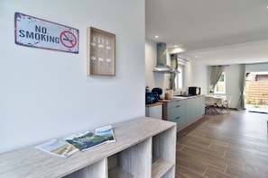 A modern kitchen with a 'NO SMOKING' sign, a wooden number lockboard, and a dining area with a table and chairs.
