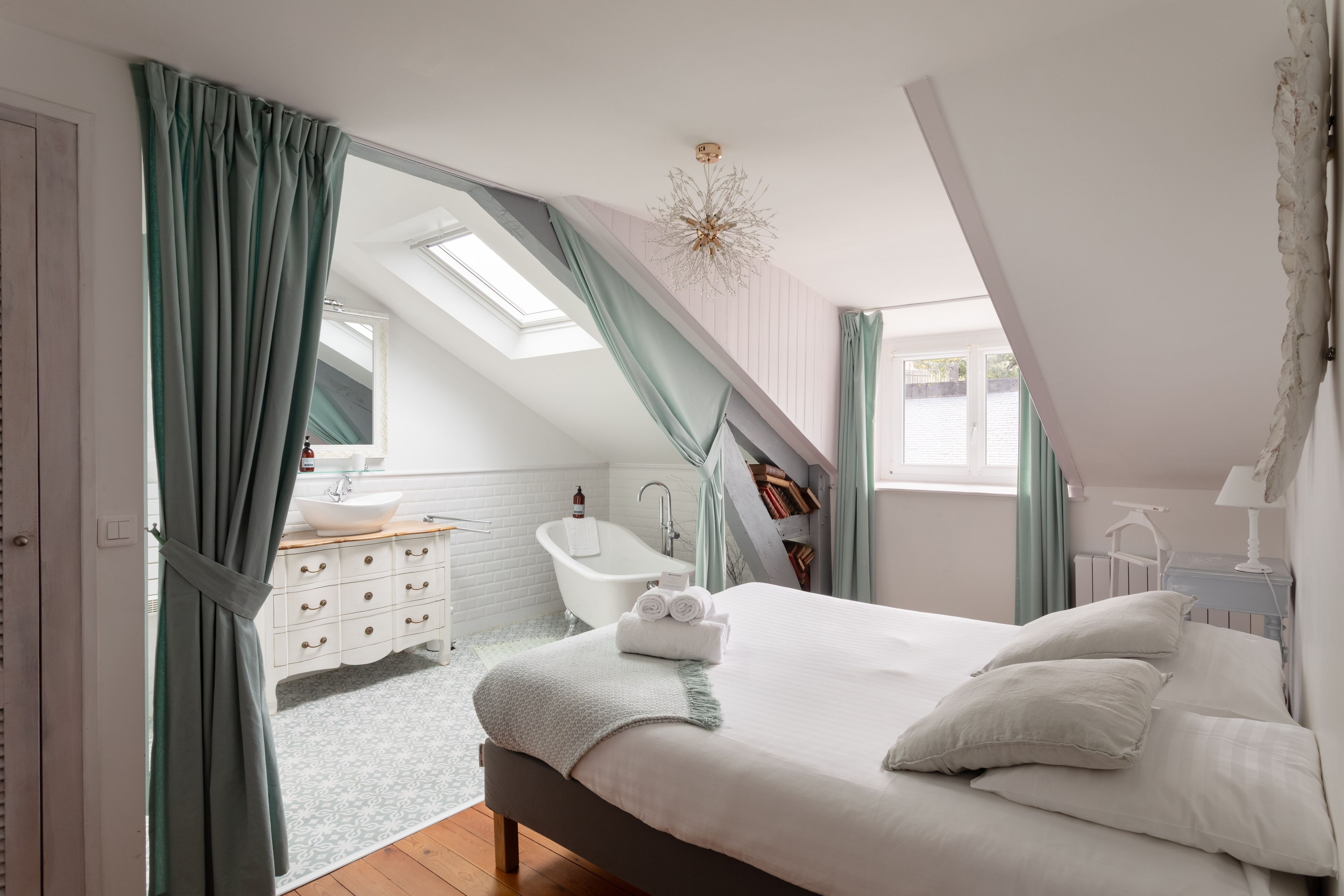 A bedroom with a large bed, a skylight, a bathroom with a bathtub, and a view of the outside.