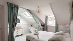 Une chambre avec un grand lit, une fenêtre de toit, une salle de bain avec baignoire et une vue sur l’extérieur.