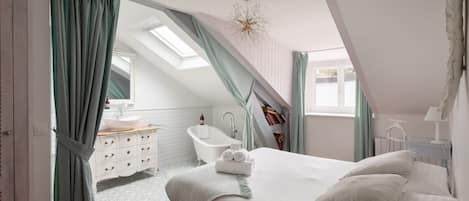 A bedroom with a large bed, a skylight, a bathroom with a bathtub, and a view of the outside.