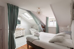 Een slaapkamer met een groot bed, dakraam, een badkamer met ligbad en uitzicht op buiten.