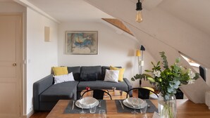 Un salon moderne avec un canapé gris, une table à manger dressée avec des assiettes et des verres, et un tableau accroché au mur.
