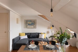 Een moderne woonkamer met een grijze bank, een eettafel gedekt met borden en glazen, en een schilderij aan de muur.