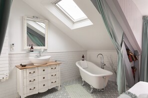 Een badkamer met een vrijstaand bad, een wastafel met lades, een spiegel en een dakraam.