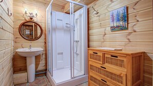 Baño de cabaña de madera con ducha envuelta en vidrio, lavabo y armario de madera.
