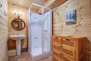 Baño de cabaña de madera con ducha envuelta en vidrio, lavabo y armario de madera.