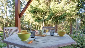 Mesa de madera al aire libre con sillas, rodeada de follaje y árboles.