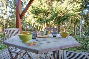 Mesa de madera al aire libre con sillas, rodeada de follaje y árboles.