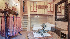 Una habitación con literas, una estatua decorativa de elefante, una escalera de madera y un espejo con un marco ornamentado.