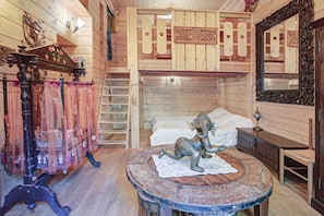 Una habitación con literas, una estatua decorativa de elefante, una escalera de madera y un espejo con un marco ornamentado.