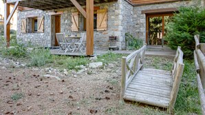 Un edificio rústico de piedra con una terraza de madera, asientos al aire libre y un puente de madera.