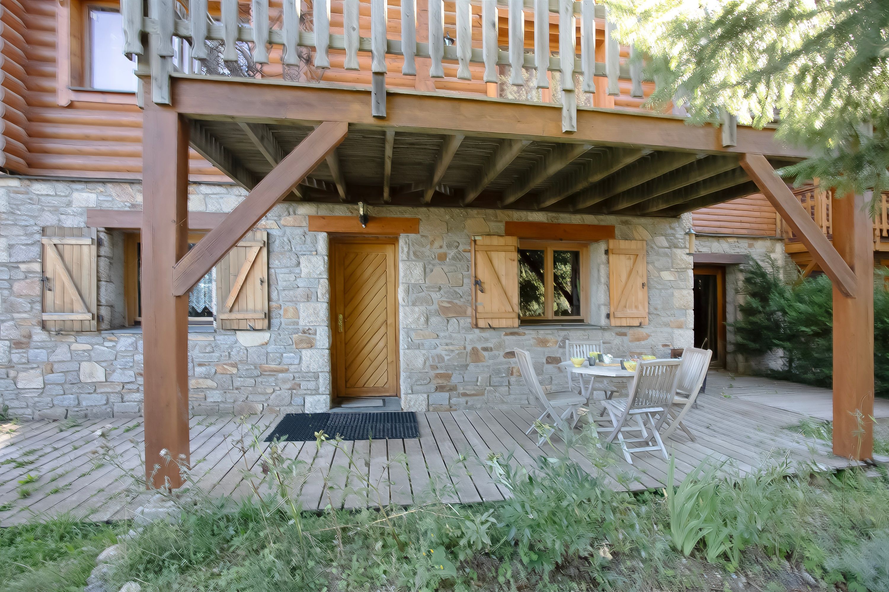 A wooden cabin with a stone exterior, a covered porch, and a table with chairs outside.