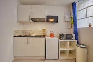 A compact kitchen with white cabinets, a built-in microwave, a small refrigerator, and a kettle on the counter. - Goshen - studio au coeur du centre historique (Bergerac)