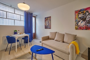 A modern living room with a sofa, a coffee table, and a dining area with a table and chairs. - Goshen - studio au coeur du centre historique (Bergerac)