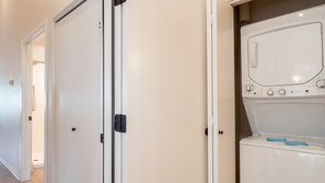 A laundry room with a washing machine and a dryer, a white door with a black handle, and a beige wall. - Pagosa Springs | Hot Tub & Mountains | 2BR Deluxe (Pagosa Springs)