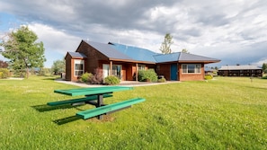 A modern building with a sloped roof, large windows, and a picnic table in the foreground. - Pagosa Springs | Hot Tub & Mountains | 3BR Sleeps 8 (Pagosa Springs)