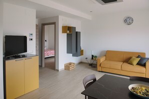 A modern living space with a television, sofa, dining table, and a small kitchen area. - Aetnamare 1: halfway between the sea and Mount Etna, with a 360° view (Mascalucia)