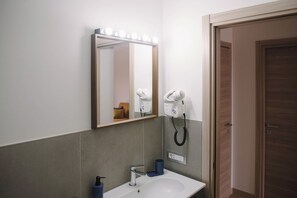 Ein Badezimmer mit Spiegel, Waschtisch und zwei an der Wand befestigten Haartrocknern.