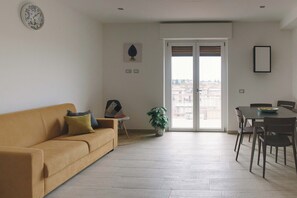 Ein Wohnzimmer mit einer Couch, einem Esstisch mit Stühlen, einer Zimmerpflanze und einer Tür, die zu einem Außenbereich führt.