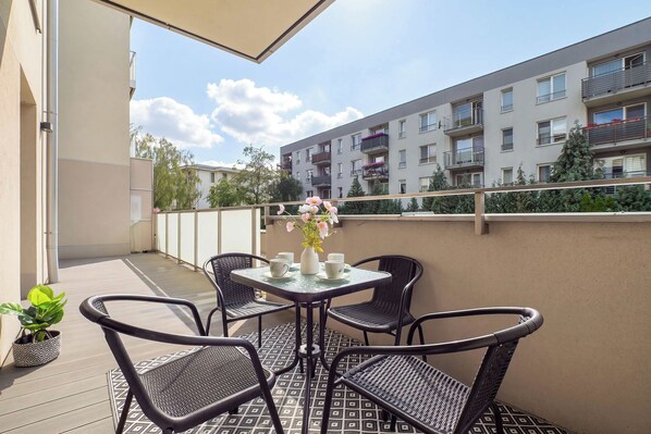 Ein Balkon mit Tisch und Stühlen, einem Blumentopf und Blick auf ein Wohngebäude.
