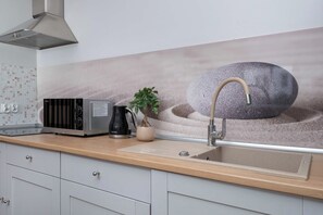 A kitchen with a modern design, featuring a stainless steel range hood, a black coffee maker, a potted plant, and a stone-like backsplash. - Łódź | Karola Borowieckiego 1 | Spacious Apartment | Terrace (Łódź)