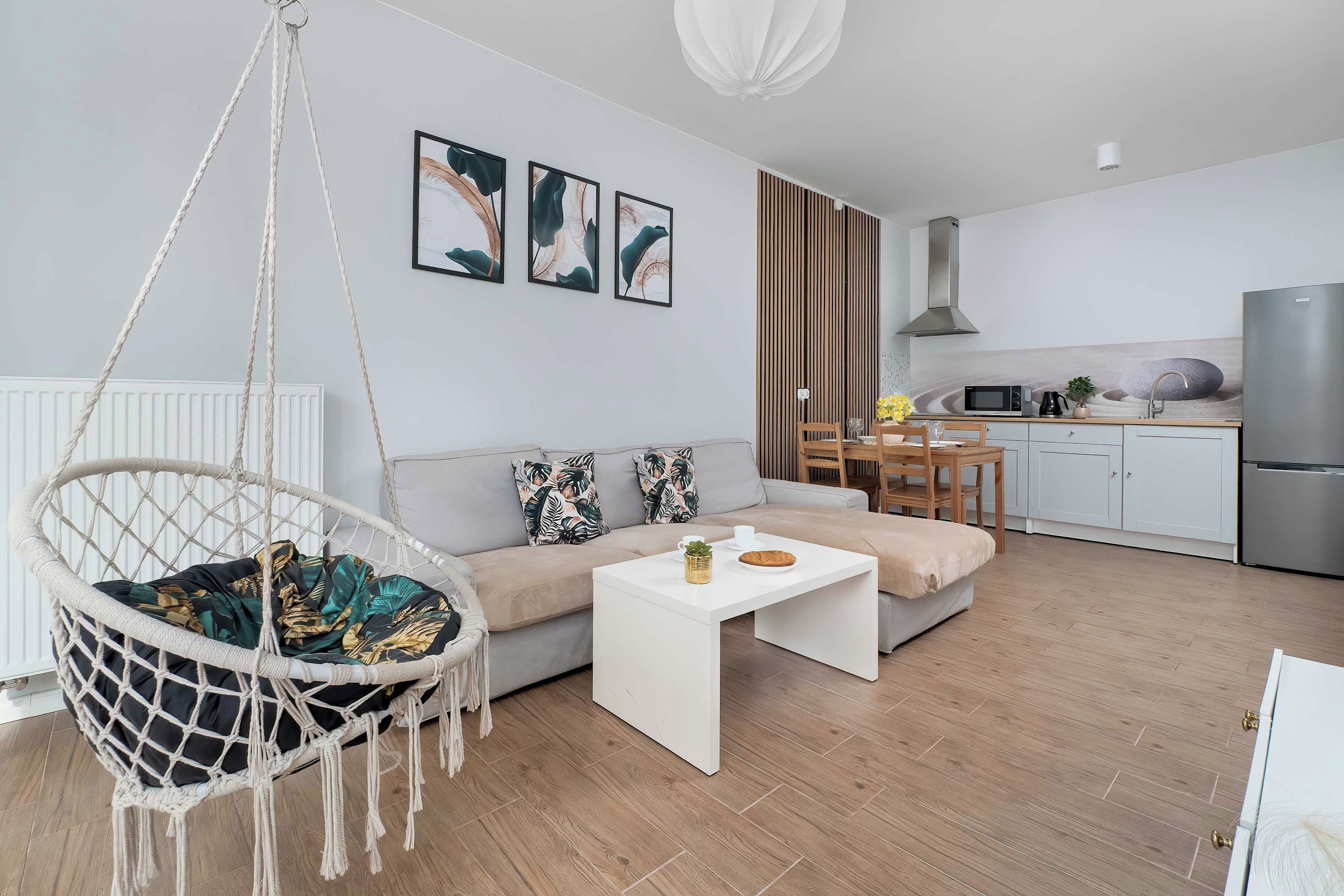 Una sala moderna con una silla colgante, un sofá, una mesa de centro y una cocina con refrigerador, microondas y pileta.