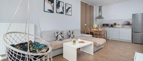 A modern living room with a hanging chair, a sofa, a coffee table, and a kitchen area with a refrigerator, microwave, and sink.