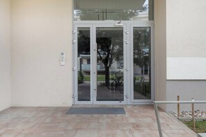 Ein Gebäudeeingang mit Glastür, Metallgitter und gefliestem Vorplatz.