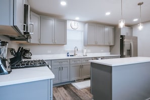 A modern kitchen with grey cabinets, a built-in stove, and a refrigerator. - Fox Lake Extended-Stay Furnished 30-Day+ Suite (Fox Lake)