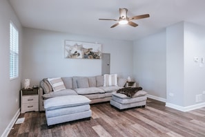 A modern living room with a sectional sofa, ottoman, and a ceiling fan. - Fox Lake Extended-Stay Furnished 30-Day+ Suite (Fox Lake)