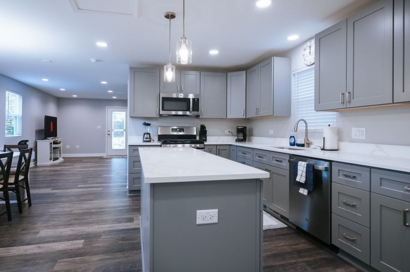 Une cuisine moderne avec des meubles gris, un îlot central, des appareils en acier inoxydable et des luminaires suspendus.