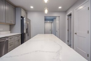 A kitchen with a marble countertop, stainless steel appliances, and a pendant light. - Fox Lake Extended-Stay Furnished 30-Day+ Suite (Fox Lake)