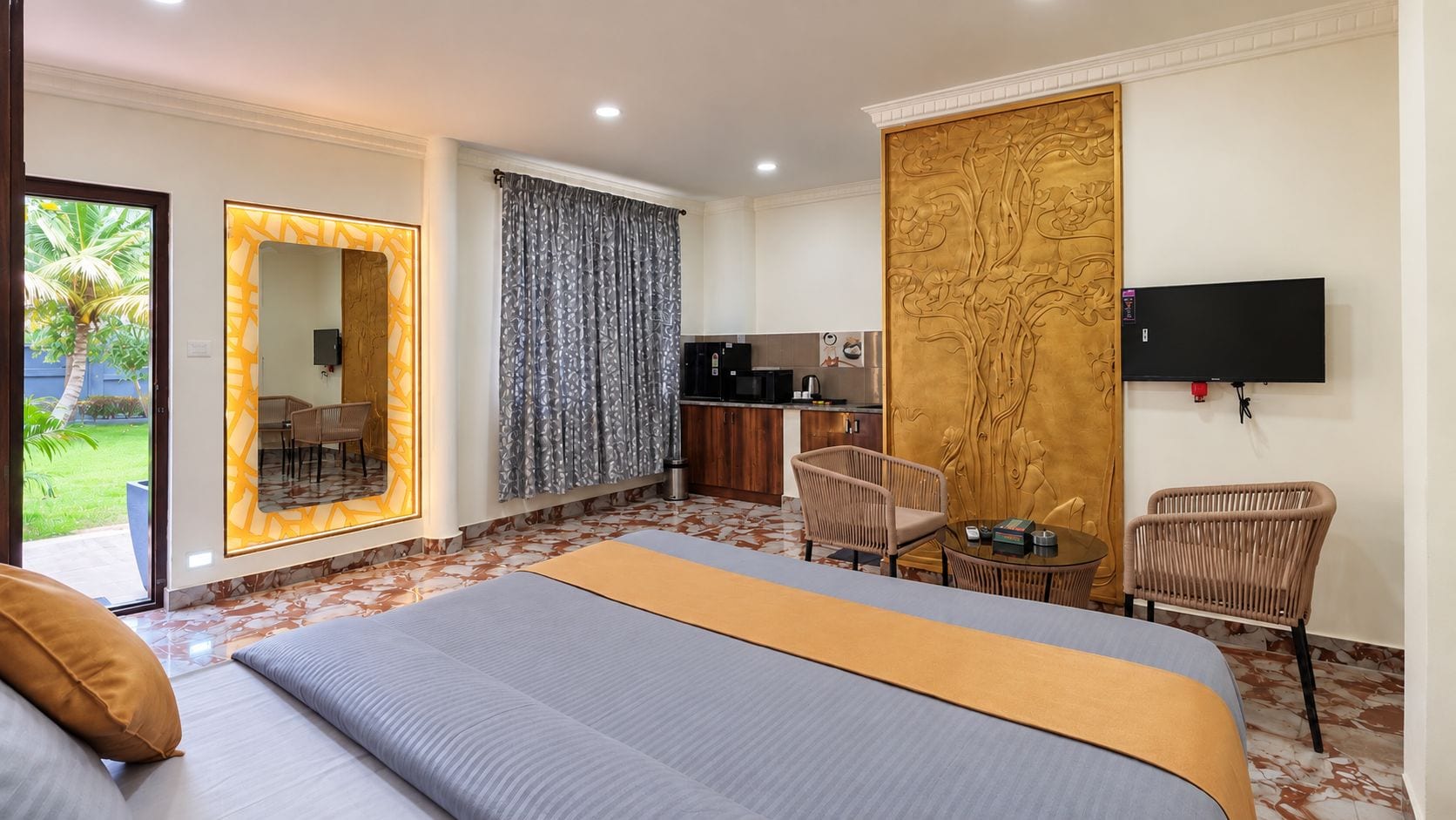 Quarto de hotel com cama, mesa de jantar, cadeiras, cozinha e televisão na parede.
