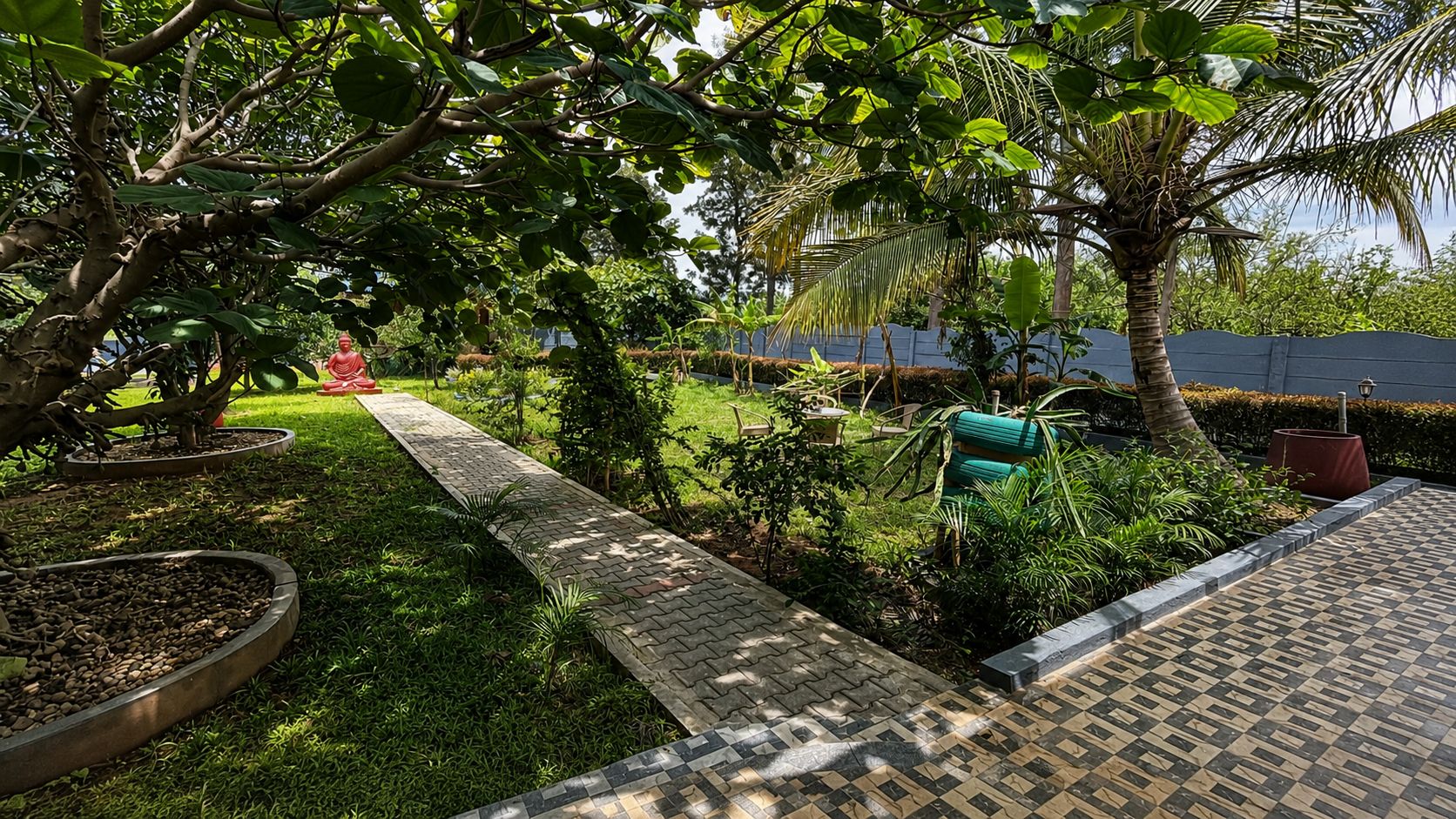 Un jardín con un camino empedrado, distintas plantas y una palmera.