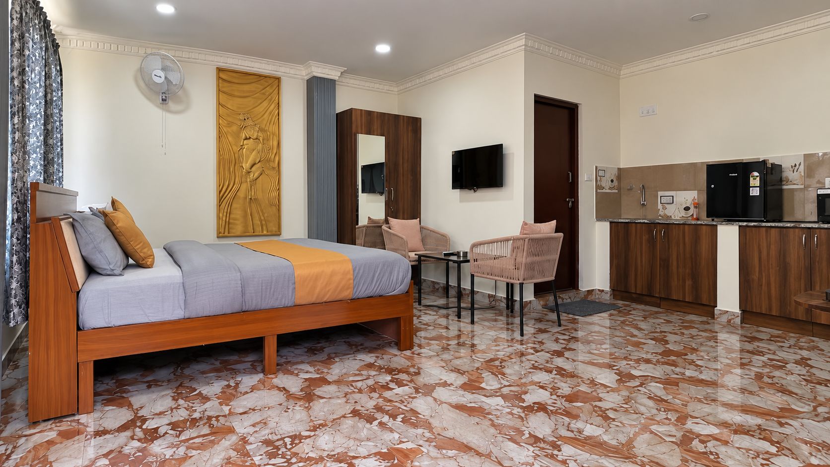 Un dormitorio con cama, escritorio, silla, televisor y un área de cocina.