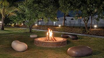 A circular fire pit with flames, surrounded by grass and large spherical stones.
