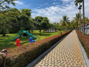 Un parque con un área de juegos, un sendero pavimentado y setos bien cuidados.