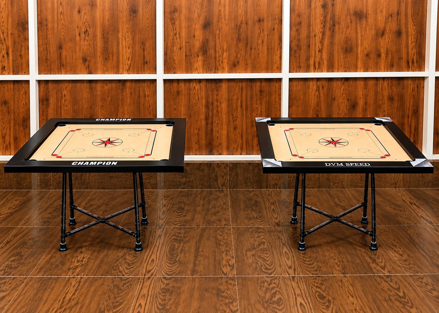 Two foosball tables with 'CHAMPION' branding, placed on a wooden floor with a white border wall in the background.