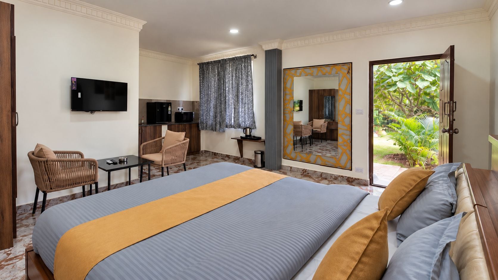 Quarto de hotel com cama, televisão, escrivaninha, cadeira, espelho e vista para o exterior.