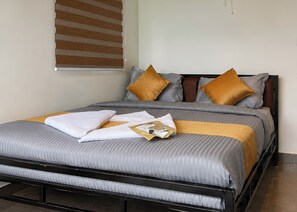 A neatly made bed with a grey and white striped bedspread, two brown pillows, and a folded white towel on the bed.