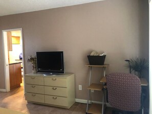 Ein Wohnzimmer mit Fernseher auf einem Schrank, einem kleinen Tisch mit einem Korb und einem Sessel.