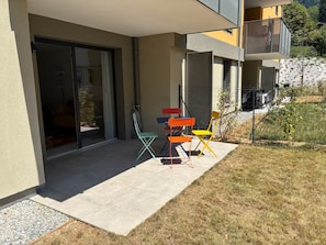 A residential building with a covered patio area, a sliding glass door entrance, and a small outdoor seating area with colorful chairs. - Les Pics Alpins (Saint Gervais)