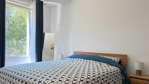 Makuuhuone, jossa on sänky, yöpöytä, lamppu ja ikkuna, jossa on verhot.