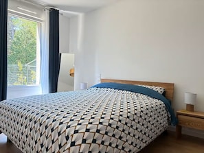 A bedroom with a bed, a nightstand, a lamp, and a window with curtains. - Les Pics Alpins (Saint Gervais)