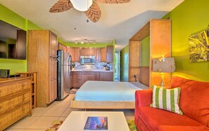 A compact living space with a kitchenette, a bed, a red sofa, and a dining area. - AVAILABLE IRONMAN 2026 - OCEANVIEW Brilliant condo Close to the PIER For Ironman (Kailua-Kona)