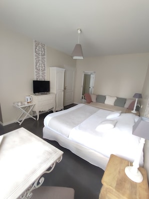 Habitación de hotel con cama, televisión, escritorio con silla, armario y mesita de noche con lámpara.