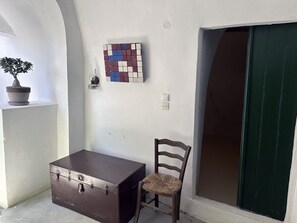 A room with a wooden chair, a brown suitcase, a potted plant, and a wall-mounted artwork.
