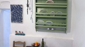 Ein Essbereich mit Tisch, Stühlen, einer Obstschüssel, einer Flasche und einem grünen Geschirrregal an der Wand.